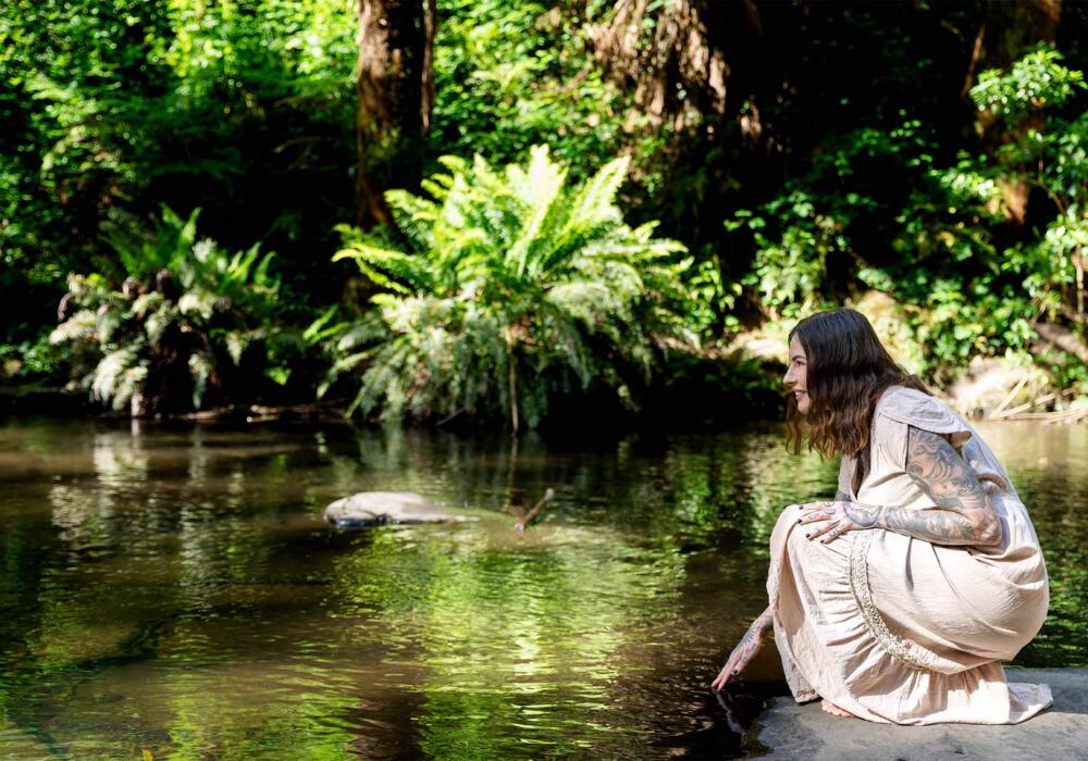 Zoe Newell, online & telehealth counsellor, kneeling at waters edge in the Otways